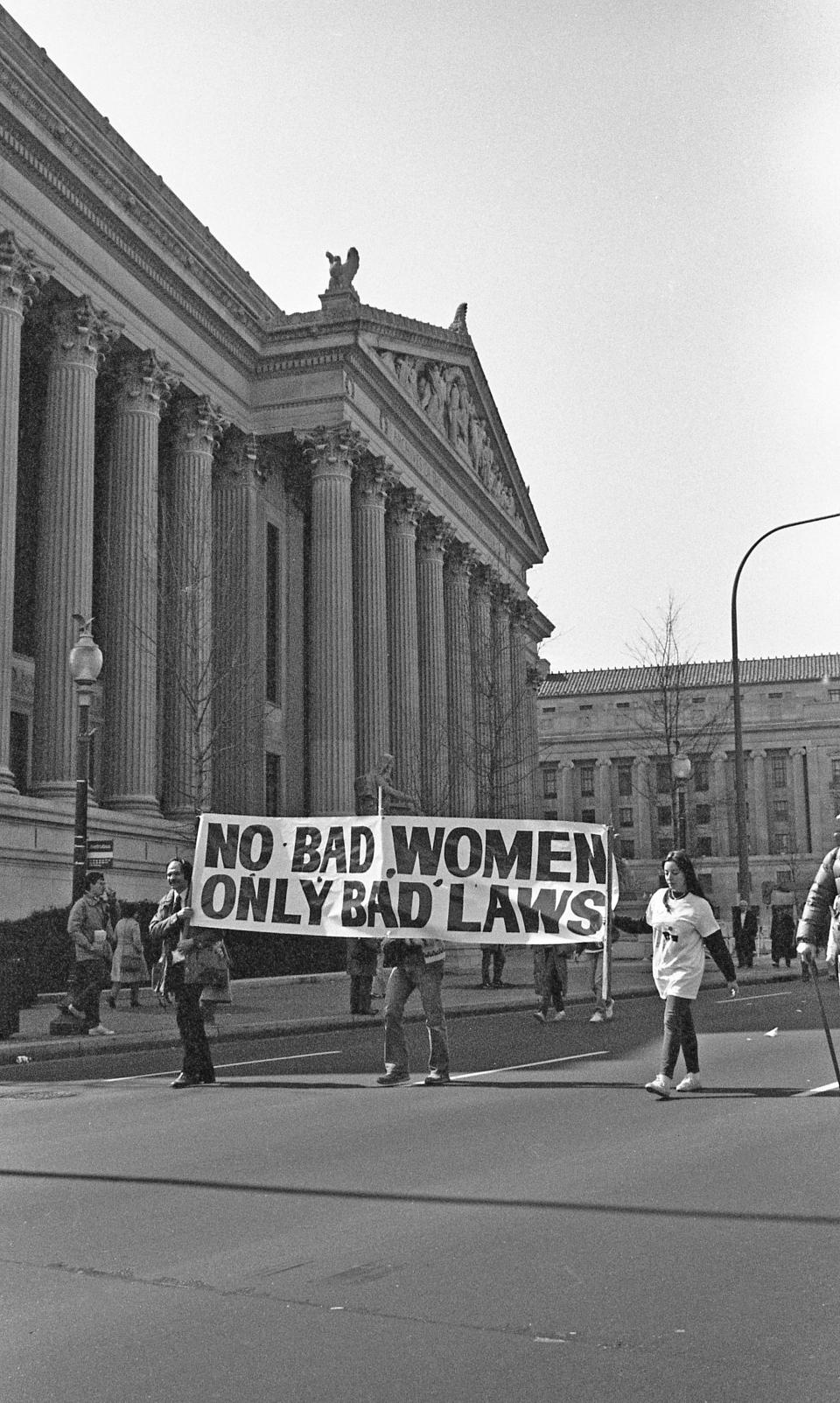 People walking in the street hold up a large banner that reads "no bad women, only bad laws"