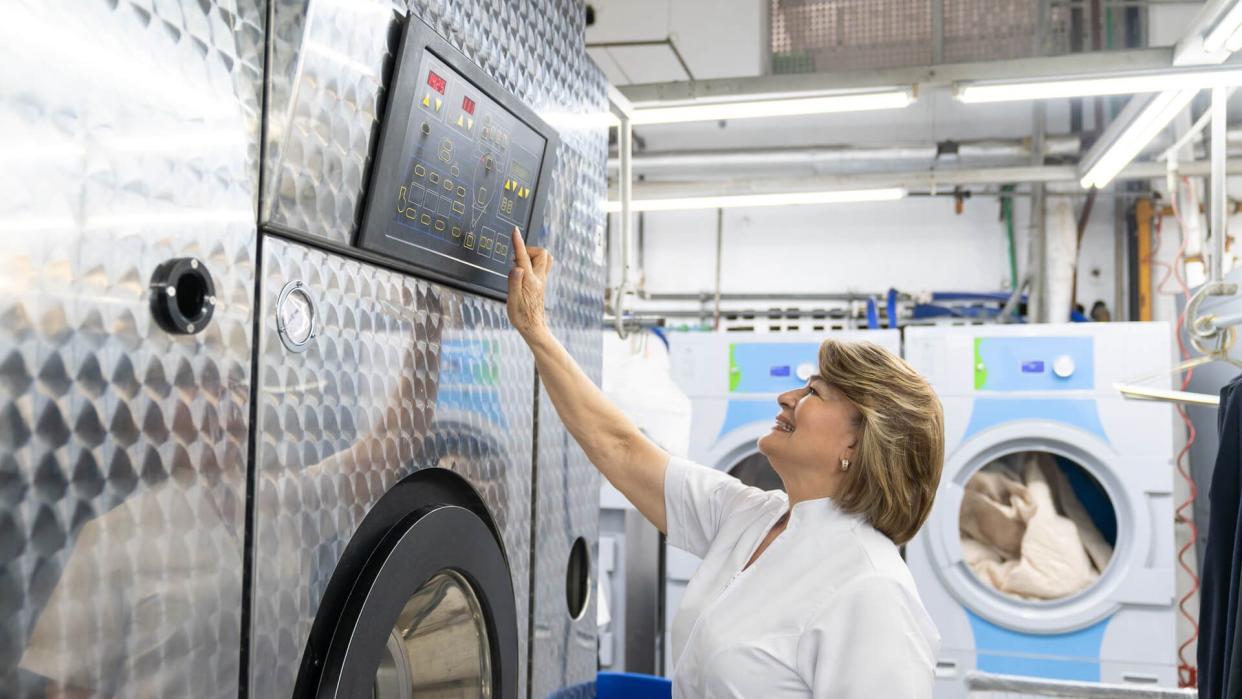 Mature woman working at a laundry service operating an industrial washing machine smiling very happy.