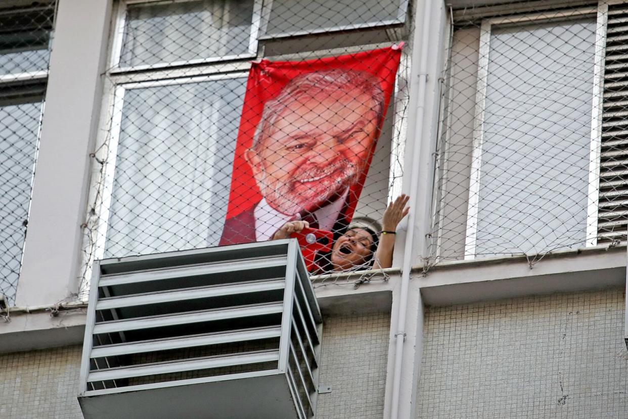 A woman holding a phone looks out the window of a building bearing a poster of a man against a red background