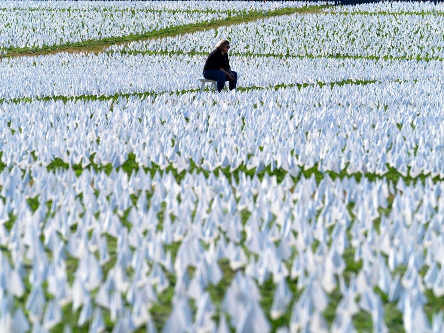 A visitor sits on a bench to look at artist Suzanne Brennan Firstenberg's "In America: Remember," a temporary art installation made up of white flags to commemorate Americans who have died of COVID-19, on the National Mall, in Washington, Saturday, Oct. 2, 2021.