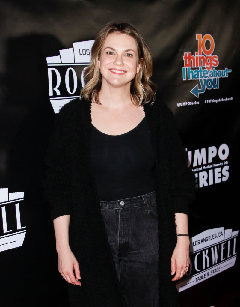 Smiling Larisa in jeans, scoop-neck top, and long coat