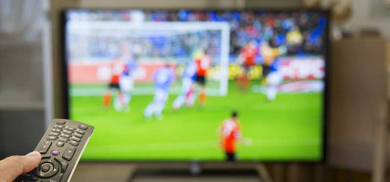 A remote is aimed at a tv showing a soccer game.