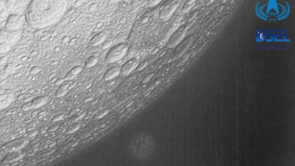 black and white image of the moon's cratered surface, with a blurry and distant earth in the background