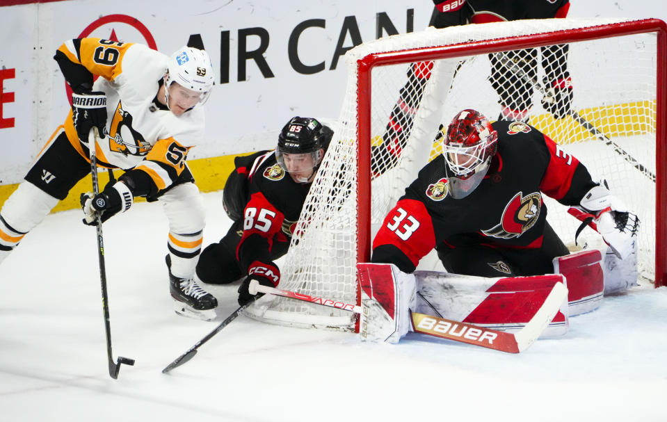 Ottawa Senators defenseman Jake Sanderson (85) tries to stop Pittsburgh Penguins left wing Jake Guentzel (59) as he wraps the puck around the net, while Senators goaltender Cam Talbot (33) covers the post during the third period of an NHL hockey game Wednesday, Jan. 18, 2023, in Ottawa, Ontario. (Sean Kilpatrick/The Canadian Press via AP)
