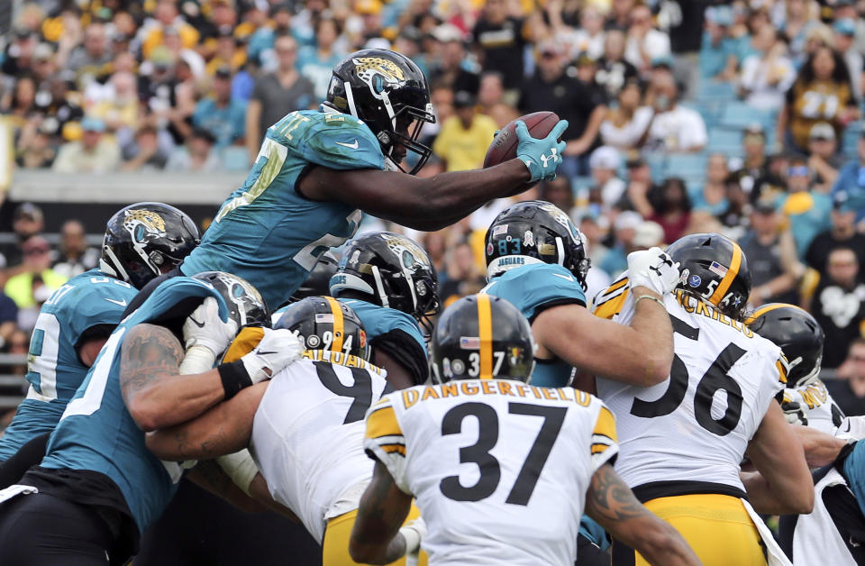 Jacksonville Jaguars running back Leonard Fournette, top, dives over the Pittsburgh Steelers defense, including Jordan Dangerfield (37) and Anthony Chickillo (56), to score a touchdown during the second half of an NFL football game, Sunday, Nov. 18, 2018, in Jacksonville, Fla. (AP Photo/Gary McCullough)