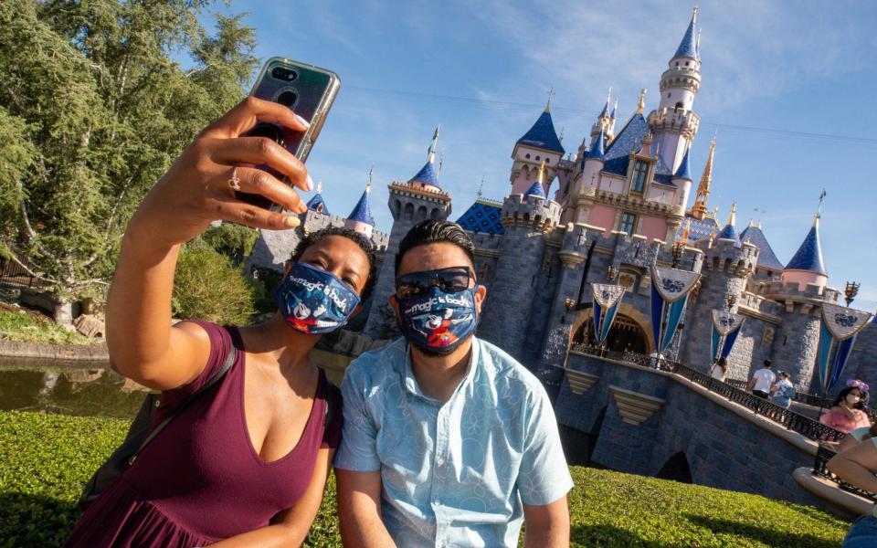 Guests in masks pose in front of Sleeping Beauty's castle at Disneyland Resort California - Handout/Getty Images