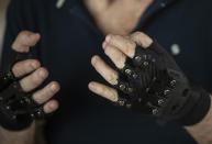 Brazilian pianist Joao Carlos Martins poses for pictures wearing bionic gloves, at his home in Sao Paulo, Brazil, Wednesday, Jan. 22, 2020. Martins, 79, was for decades Brazil's most acclaimed pianist, but an accident an a degenerative disease forced him to stop playing with both hands since 1998. That changed a few months ago when a new friend came to him with a pair bionic gloves that suit him perfectly. He can now play again with nine out of ten fingers. (AP Photo/Andre Penner)