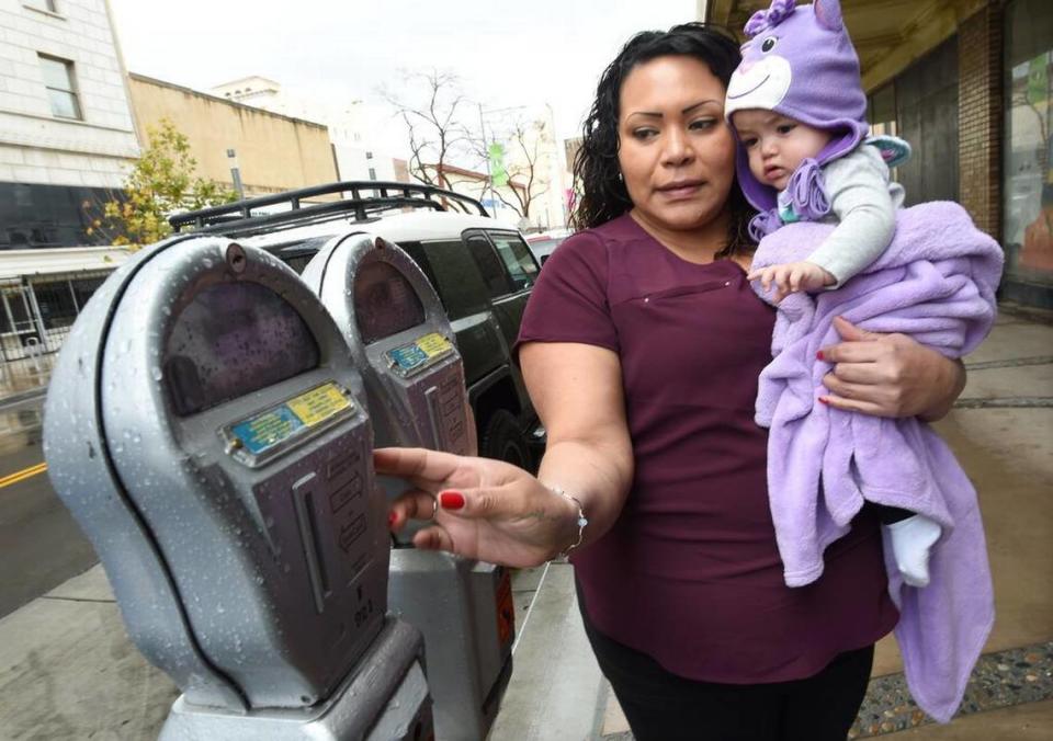 Josephine Smith feeds coins into her parking meter, with her 10-month-old daughter, Mia Castillo, on Fulton Street in downtown Fresno, Friday Feb. 15, 2019. The City of Fresno is taking steps to upgrade existing parking meters downtown to install smart meters.