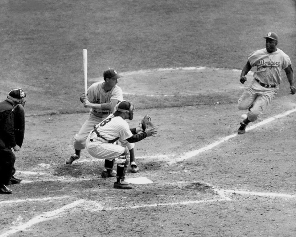 Jackie Robinson of the Dodgers steals home in game 1 of the 1955 World Series against the Yankees, with Yogi Berri behind the plate.