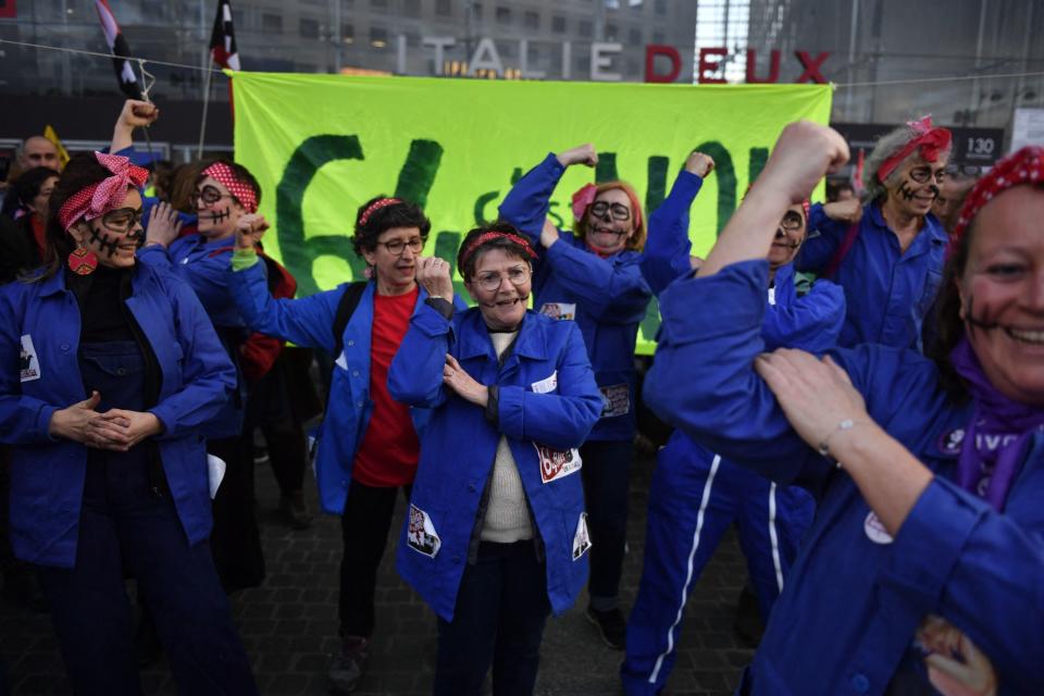 Feminist collective members wear jackets with patches and bandanas tied around their heads hold their arms up in the "Rosie the Riveter" pose with their faces painted like skeletons