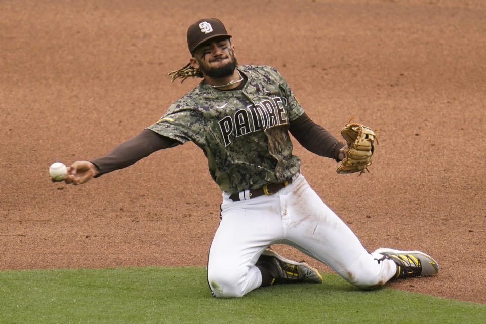 San Diego Padres shortstop Fernando Tatis Jr., throws to first from his knees in time for the out on San Francisco Giants' Wilmer Flores during the fifth inning of a baseball game Sunday, May 2, 2021, in San Diego. San Francisco Giants Tommy La Stella scored from third on the play. (AP Photo/Gregory Bull)