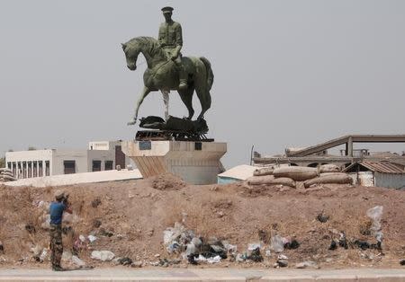 A Kurdish fighter from the People's Protection Units (YPG) fires his weapon at a statue of Bassel al-Assad, brother of Syria's President Bashar, in the Ghwairan neighborhood of Hasaka, Syria, August 22, 2016.REUTERS/Rodi Said