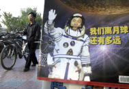 In this photo taken Thursday, Oct 23, 2003, a man pushes his bicycle past the cover of a magazine showing China's first man in space, Yang Liwei and the Chinese characters for "How far are we from the moon?" at a newsstand in Beijing, China. China's Nov. 24, 2020, trip to the moon and, presumably, back is the latest milestone in the Asian powerhouse's slow but steady ascent to the stars. (AP Photo/Ng Han Guan, File)