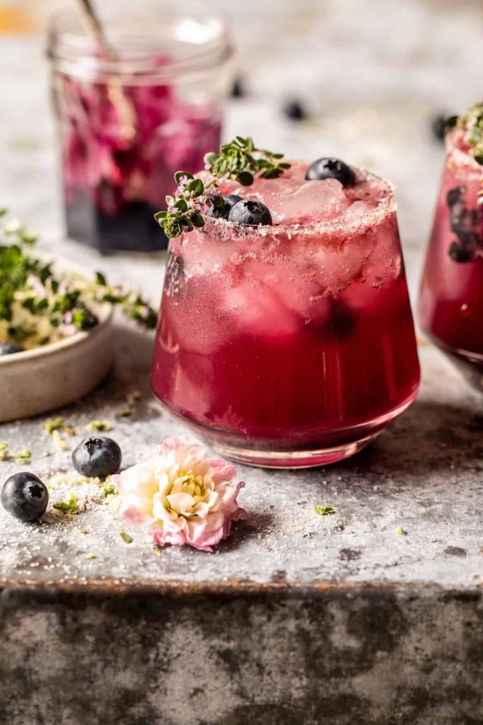 A blueberry cocktail garnished with fresh thyme.