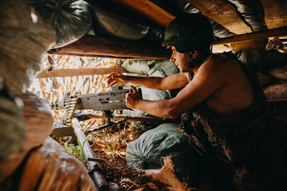 A Ukrainian soldier in a helmet and no shirt in a dugout, handling artillery.