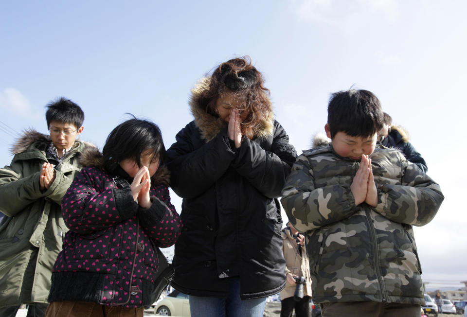 A family observes a moment of silence in front of what is left of a disaster control center in an area devastated by the March 11, 2011 earthquake and tsunami, in Minamisanriku, Miyagi prefecture, Japan, Sunday, March 11, 2012. Through silence and prayers, people across Japan on Sunday remembered the massive earthquake and tsunami that struck the nation one year ago, killing just over 19,000 people and unleashing the world's worst nuclear crisis in a quarter century. (AP Photo/Shizuo Kambayashi)