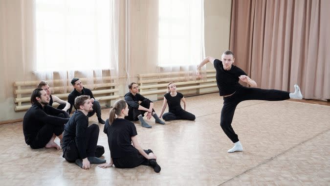 Young man wearing black outfit showing contemporary dance move to his team, horizontal shot.