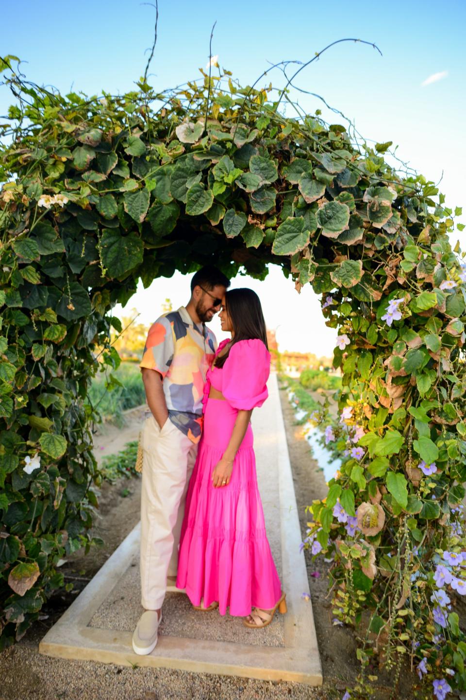 A man and woman lean their heads together under a greenery archway.