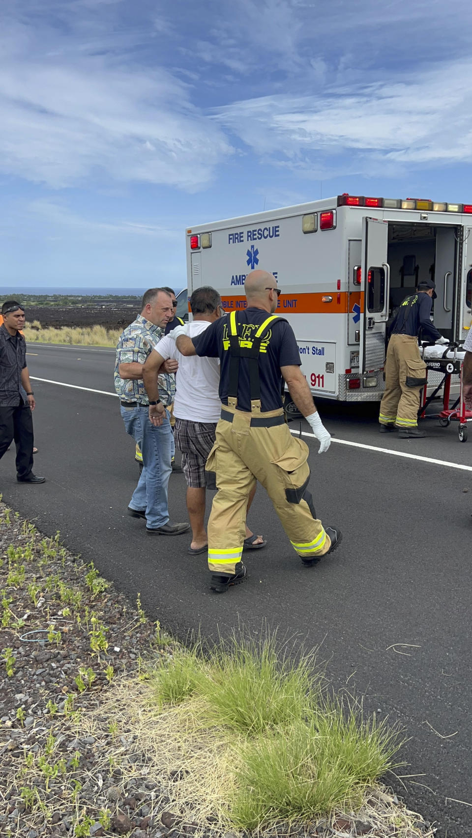 Hawaii Gov. Josh Green, second left, assists an injured driver at the scene of an overturned vehicle in Waikoloa, Hawaii, Thursday, May 18, 2023. Gov. Green, who is also a physician, was one of the people who stopped to help when his security detail spotted a vehicle upside down in a lava field Thursday while en route to a Big Island event. The man who was wearing a seatbelt, had a few cuts and bruises and seemed to be OK, Green said. (Reece Kainoa Kilbey/Office of the Governor, State of Hawai'i via AP)