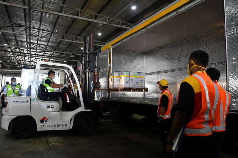 Workers load containers carrying the first batch of Pfizer-BioNTech COVID-19 vaccines into a truck at the MASkargo Complex in Sepang