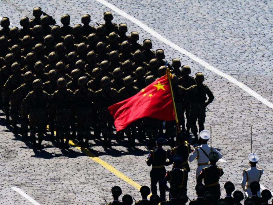 Chinese soldiers march with Chinese flag in foreground during a military parade