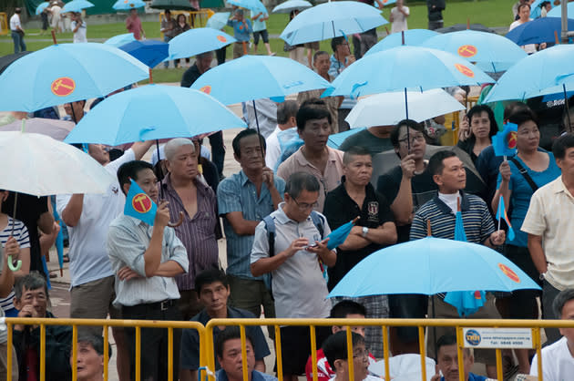 Workers' Party supporters huddle under a cluster of blue umbrellas when a slight drizzle rains upon the field, minutes before the rally begins. (Yahoo! photo)