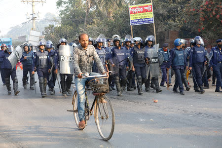 A commuter rides a bicycle while police chase garments workers who have been protesting for higher wages at Ashulia, outskirt of Dhaka, Bangladesh, January 14, 2019. REUTERS/Mohammad Ponir Hossain