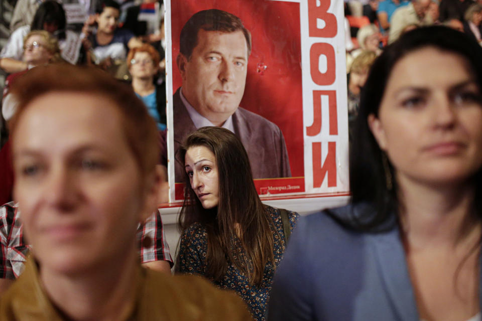 FILE- A woman stands next to a poster of Milorad Dodik at an election rally of the "Alliance of Independent Social Democrats" party in the Bosnian town of Banja Luka, on Sept. 29, 2016. Long-reigning Bosnian Serb leader, Milorad Dodik, has grown increasingly hostile this week as the West turned up the pressure on him to stop a spiraling secessionist campaign in his multiethnic Balkan country of 3.3 million people that has never truly recovered from its fratricidal 1992-95 war. (AP Photo/Amel Emric, File)