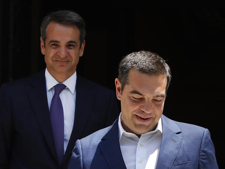 Greece's newly-elected prime minister Kyriakos Mitsotakis, background, looks on as outgoing prime minister Alexis Tsipras, leaves the Maximos Mansion in Athens, Monday, July 8, 2019. Mitsotakis' New Democracy party won 39.8% of the vote, giving him 158 seats in the 300-member parliament, a comfortable governing majority. (AP Photo/Thanassis Stavrakis)