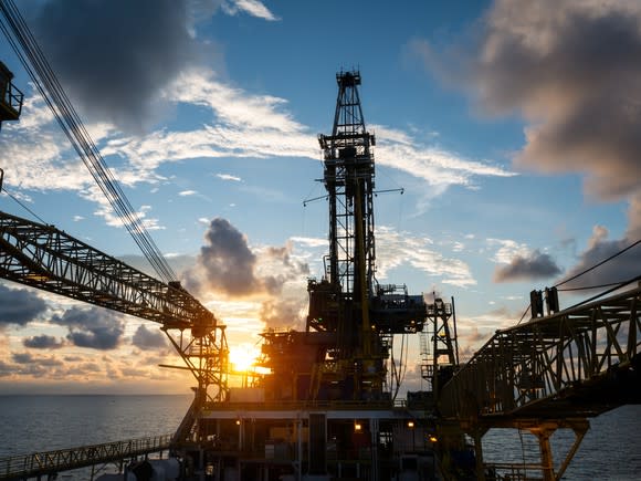 An offshore drilling rig with the sun rising behind it.