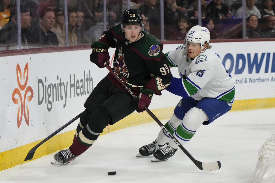 Arizona Coyotes defenseman J.J. Moser (90) and Vancouver Canucks center Sheldon Dries race for the puck during the second period of an NHL hockey game Thursday, April 13, 2023, in Tempe, Ariz. (AP Photo/Rick Scuteri)