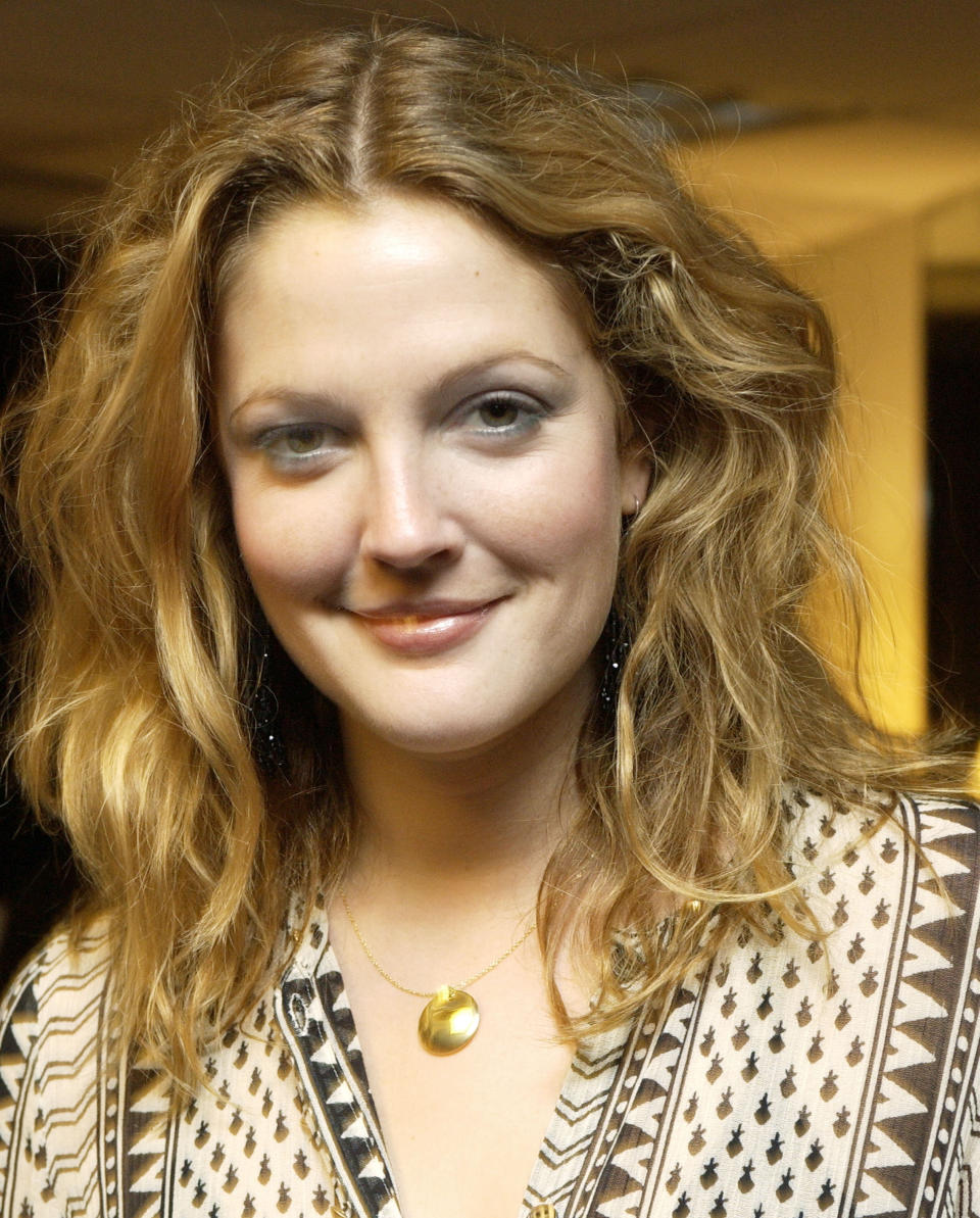 Drew Barrymore smiles softly, wearing a printed top with a round pendant necklace