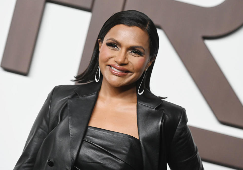 Mindy Kaling wearing a leather jacket and matching outfit, smiles at a red carpet event