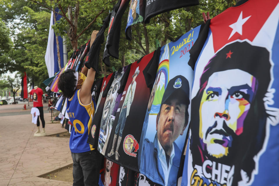 A vendor sells T-shirts promoting Nicaraguan President Daniel Ortega and The Sandinista National Liberation Front ruling party on the sidelines of a new monument, called the Peace Bell, before its inauguration ceremony later in the day in Managua, Nicaragua, Friday, July 17, 2020. Nicaraguan President Daniel Ortega's government is being deterred by the new coronavirus from holding the usual mass celebration to mark the victory of the country's revolution July 19, and will instead unveil a new addition to its collection of monuments. At right is a T-shirt of Cuba's revolutionary hero Ernesto "Che" Guevara. (AP Photo/Alfredo Zuniga)