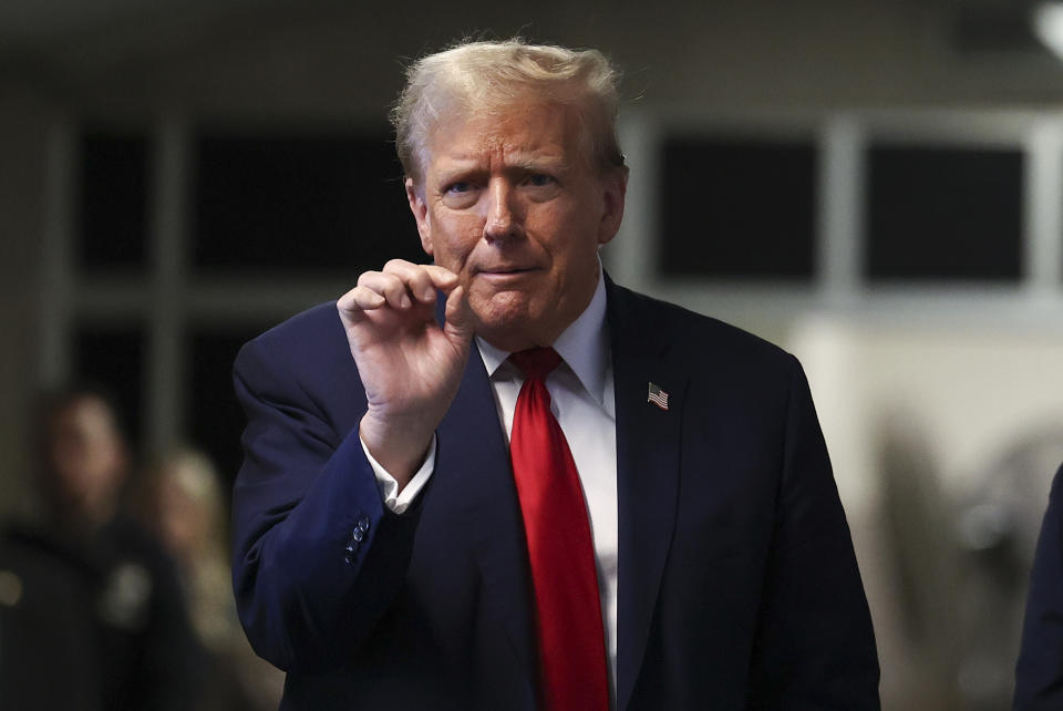 Donald Trump in a suit gestures with his right hand, looking forward