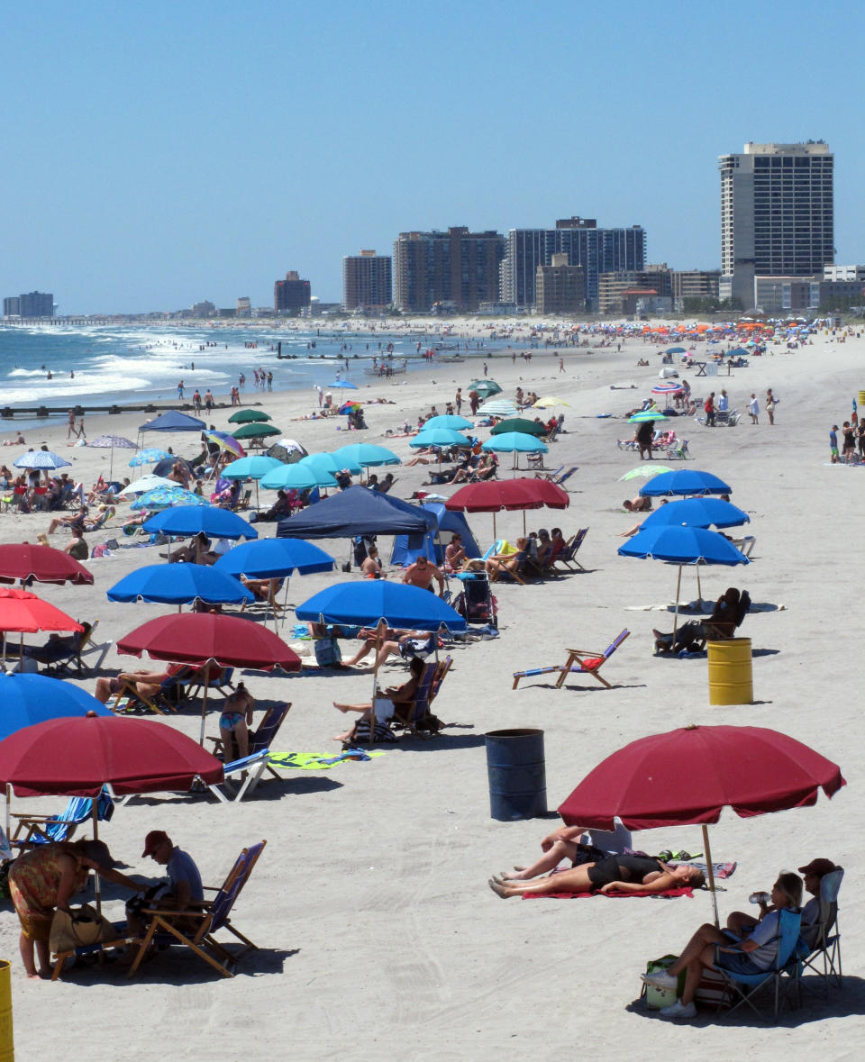 In this July 9, 2018 photo, beach-goers huddle under beach umbrellas on the sand in Atlantic City, N.J. The New Jersey Legislature is considering a bill in February 2020 to require beach umbrellas to be tethered to the sand to prevent injuries from flying umbrellas. (AP Photo/Wayne Parry)