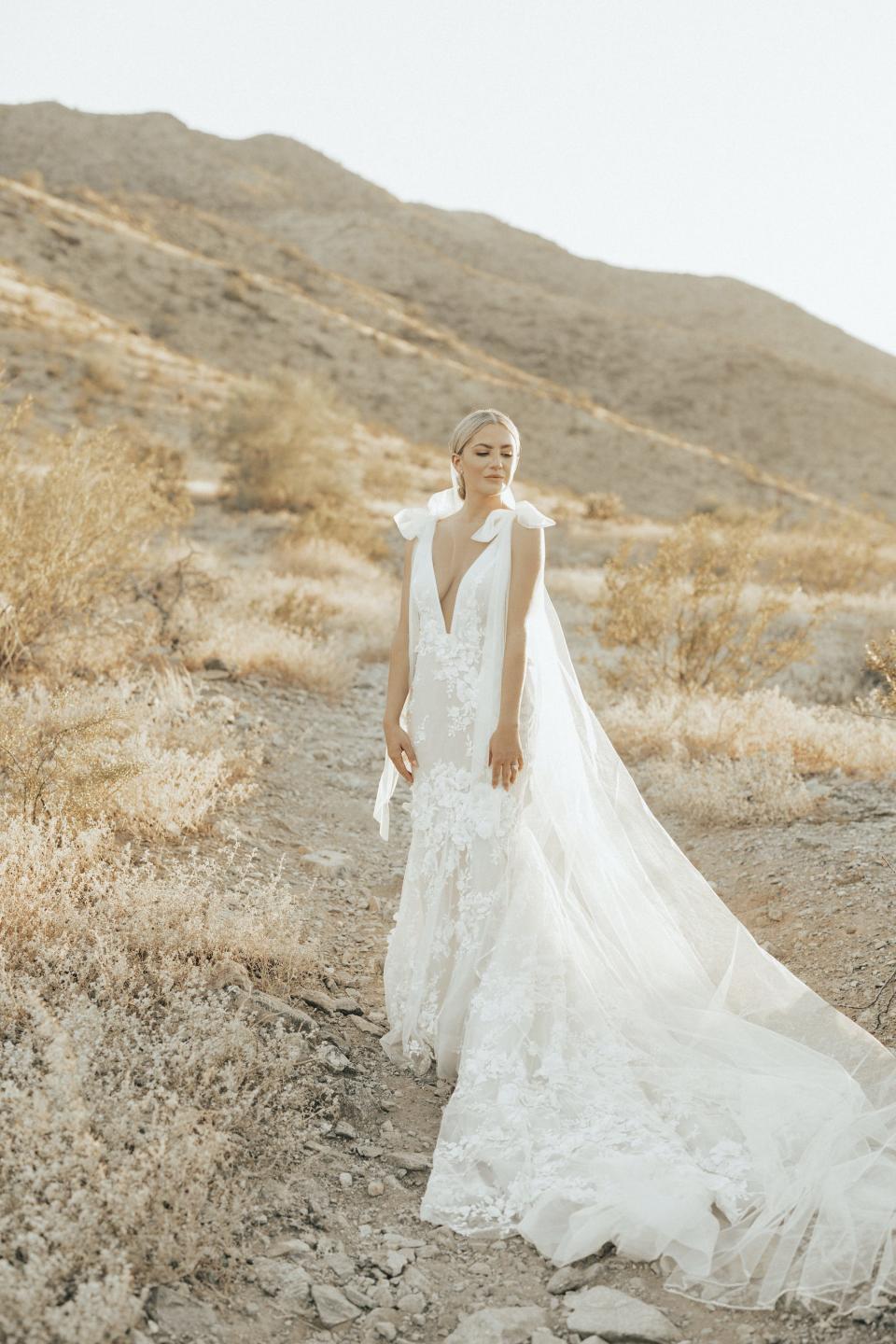 A bride looks off into the distance in her wedding dress in front of a hilly background.