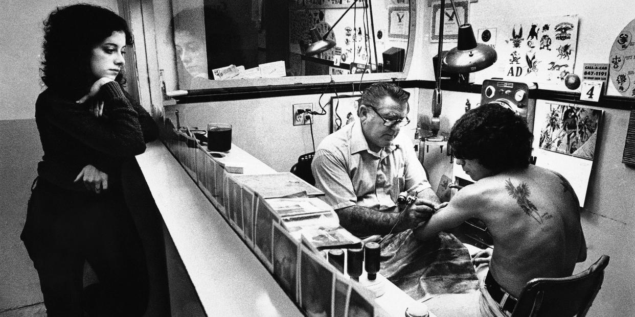 A woman watches a client get inked at a tattoo shop in 1984 in Rhode Island