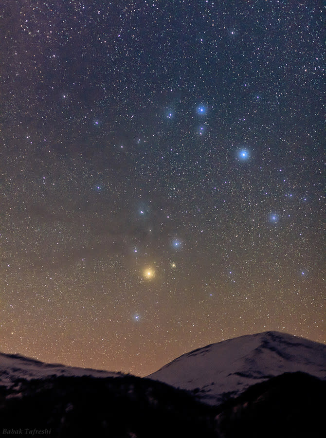 a bright red star amidst a filed of stars in the night sky visible above a few mountain peaks
