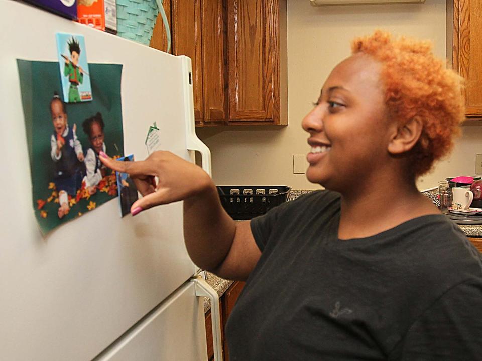 Jasmine Kirk points to a photograph of herself and her sister as children that hangs on the refrigerator in her kitchen in her home in Akron.