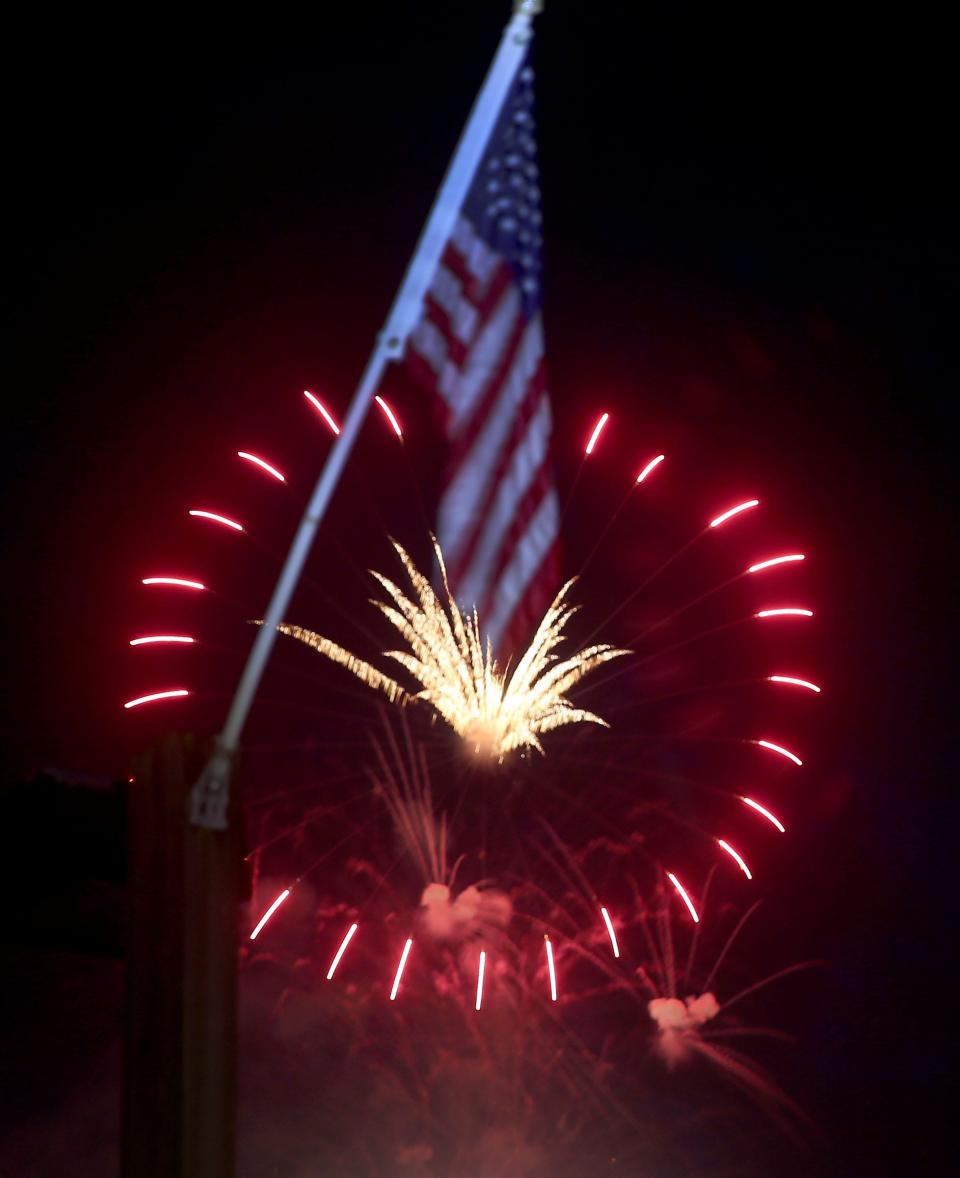 Fireworks over the Toms River explode behind a flag at the Riverfront Marina in Beachwood.