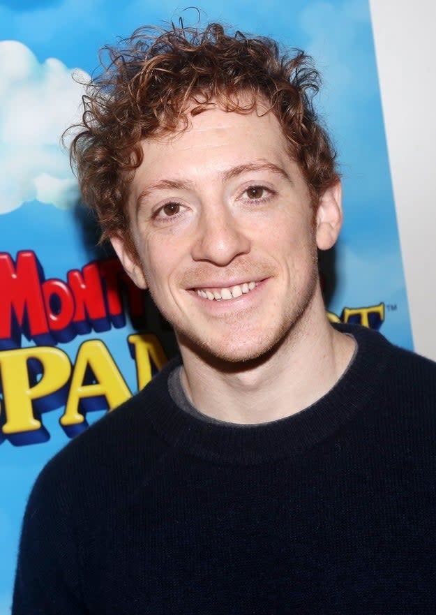 A smiling person with curly hair in front of a banner for the movie 