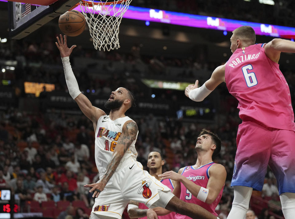 Miami Heat forward Caleb Martin (16) goes up for a shot past Washington Wizards forward Will Barton (5) and center Kristaps Porzingis (6) during the first half of an NBA basketball game, Wednesday, November 23, 2022, in Miami. (AP Photo/Jim Rassol)