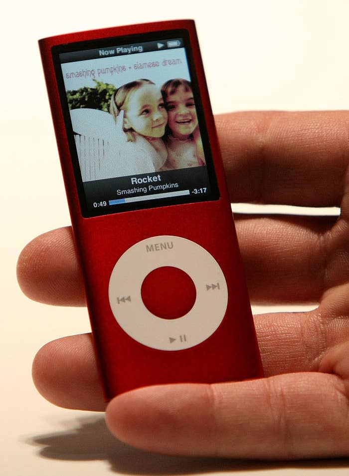 Hand holding a red iPod nano displaying a photo of two smiling children with "Smashing Pumpkins - 1979" on screen