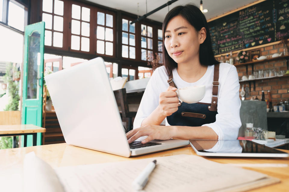 A female cafe owner looks at business information on a laptop.