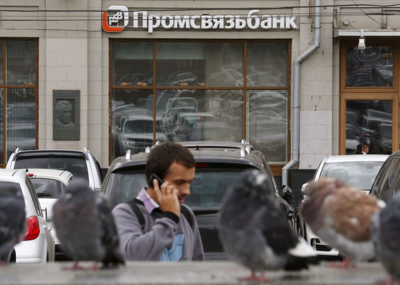 Man speaks on the phone near pigeons, with a branch of Promsvyazbank seen in the background, in Moscow