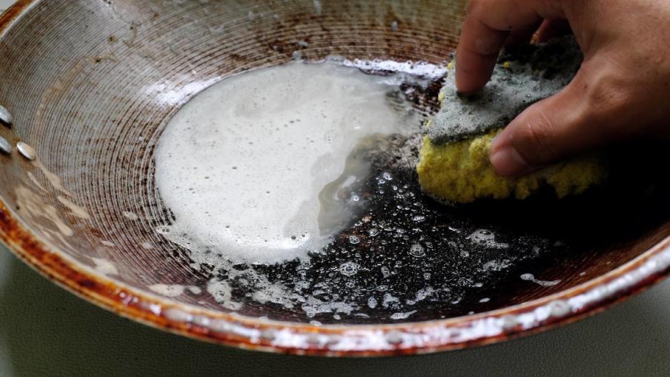 How to clean a wok: Human hand scrubbing or cleaning a burnt, scorched and greasy pan or wok on kitchen sink. 