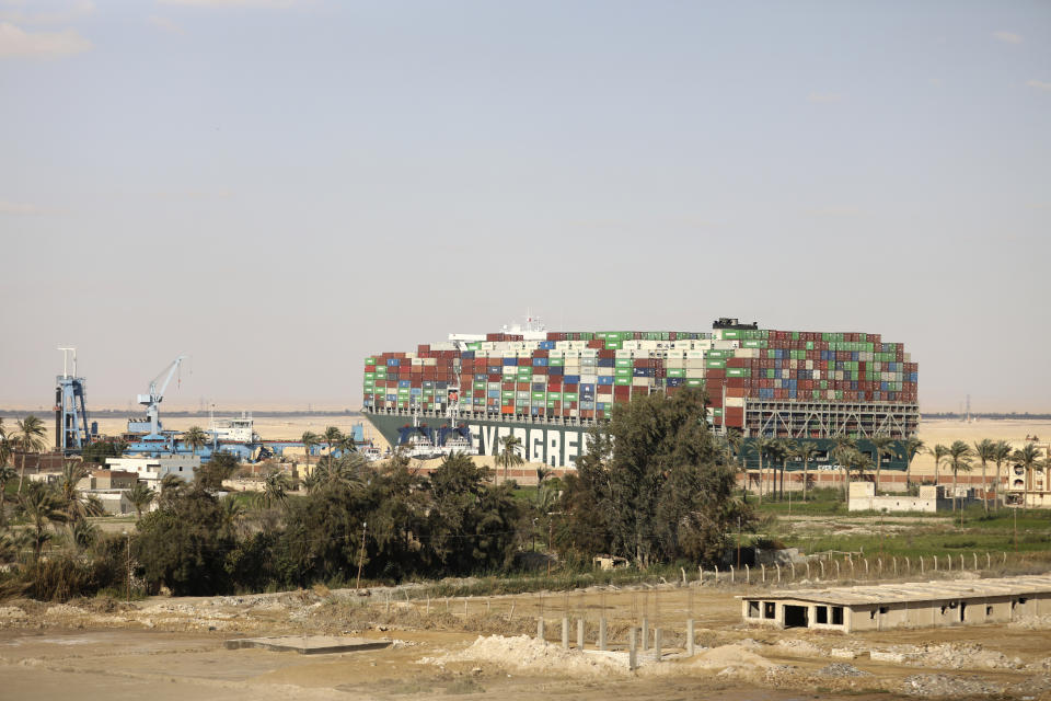 FILE - The Ever Given, a Panama-flagged cargo ship wedged across the Suez Canal and blocking traffic looms over the village of Amer, near Suez, Egypt on March 28, 2021. The world’s biggest shipping company said Monday Feb. 13, 2023 it sued a rival shipping line in a Danish court, seeking compensation for ship delays that resulted from the blocking of the Suez Canal by a hulking vessel two years ago. (AP Photo/Mohamed Elshahed, File)