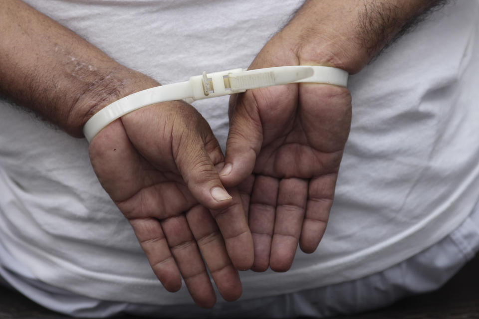 A handcuffed man, arrested for alleged gang connections, waits to be transferred to a prison at the police delegation of San Bartolo in Soyapango, El Salvador, Tuesday, Aug. 16, 2022. The government of Salvadoran President Nayib Bukele asked Congress on Tuesday to approve a fifth extension of the state of emergency to continue fighting gangs, on the same day that a group of people demanded in the streets the freedom of imprisoned relatives. (AP Photo/Salvador Melendez)