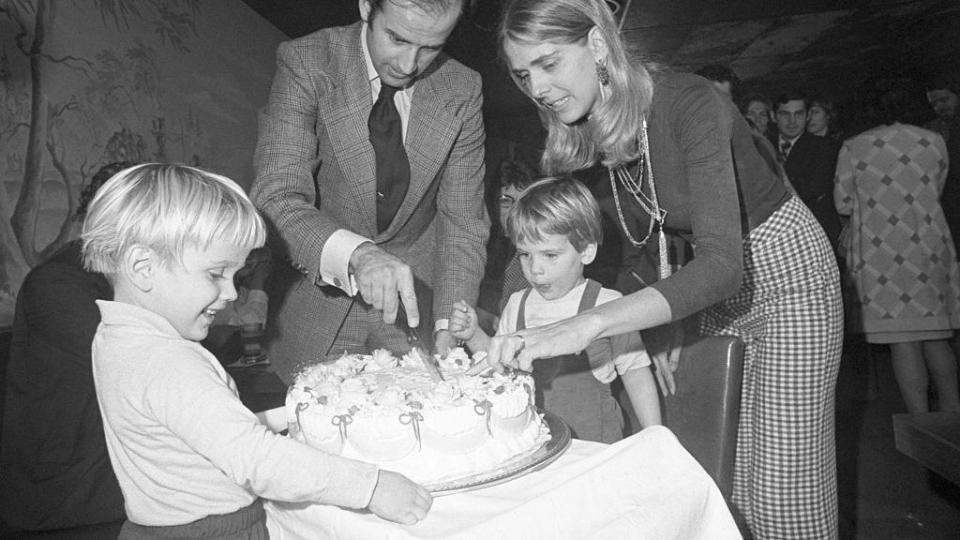 a black and white photo of joe and nelia biden cutting a piece of cake while hunter biden looks on and another child stands near the table